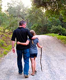 Andrew Tanis walking down the road with his daughter. The road stretches out ahead of them.